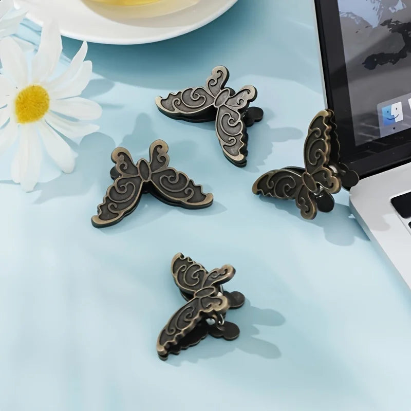 A collection of vintage butterfly metal book clips resting on a light blue surface next to a laptop.