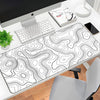 A large contoured rubber mouse pad with a black and white topographic line design is placed on a desk next to a computer moni