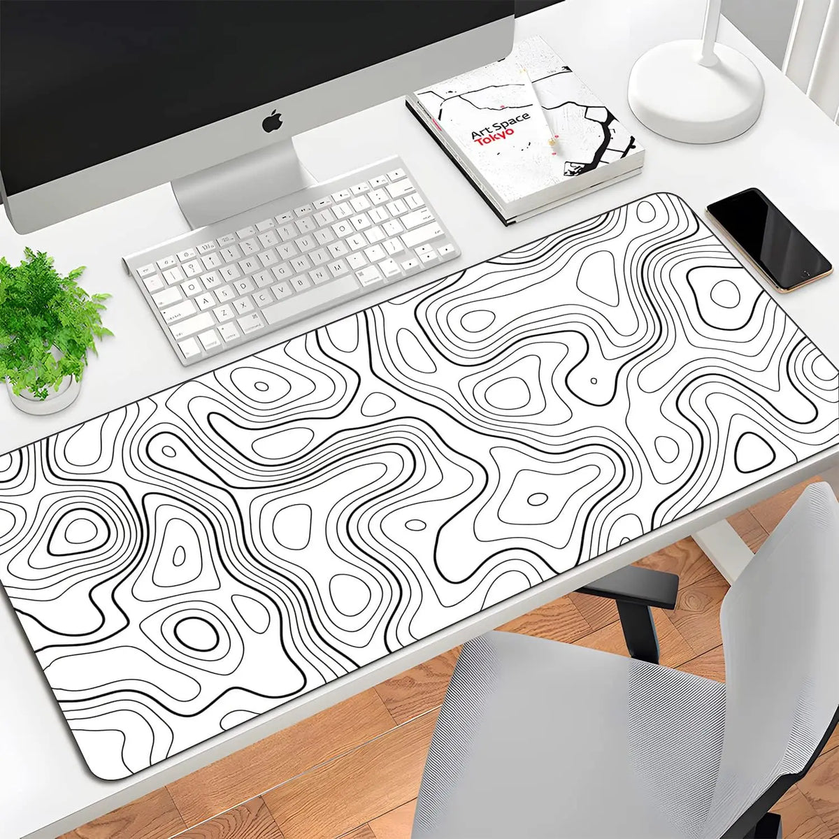 A large contoured rubber mouse pad with a black and white topographic line design is placed on a desk next to a computer moni