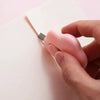 A hand holds a pink utility knife with a rounded grip, positioned next to a white piece of paper.