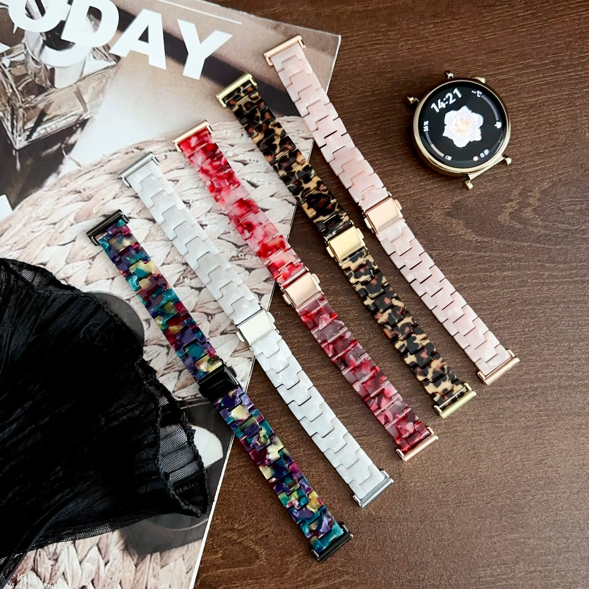 A collection of resin beaded watch bands in various colors and patterns laid out on a wooden surface next to a wristwatch.