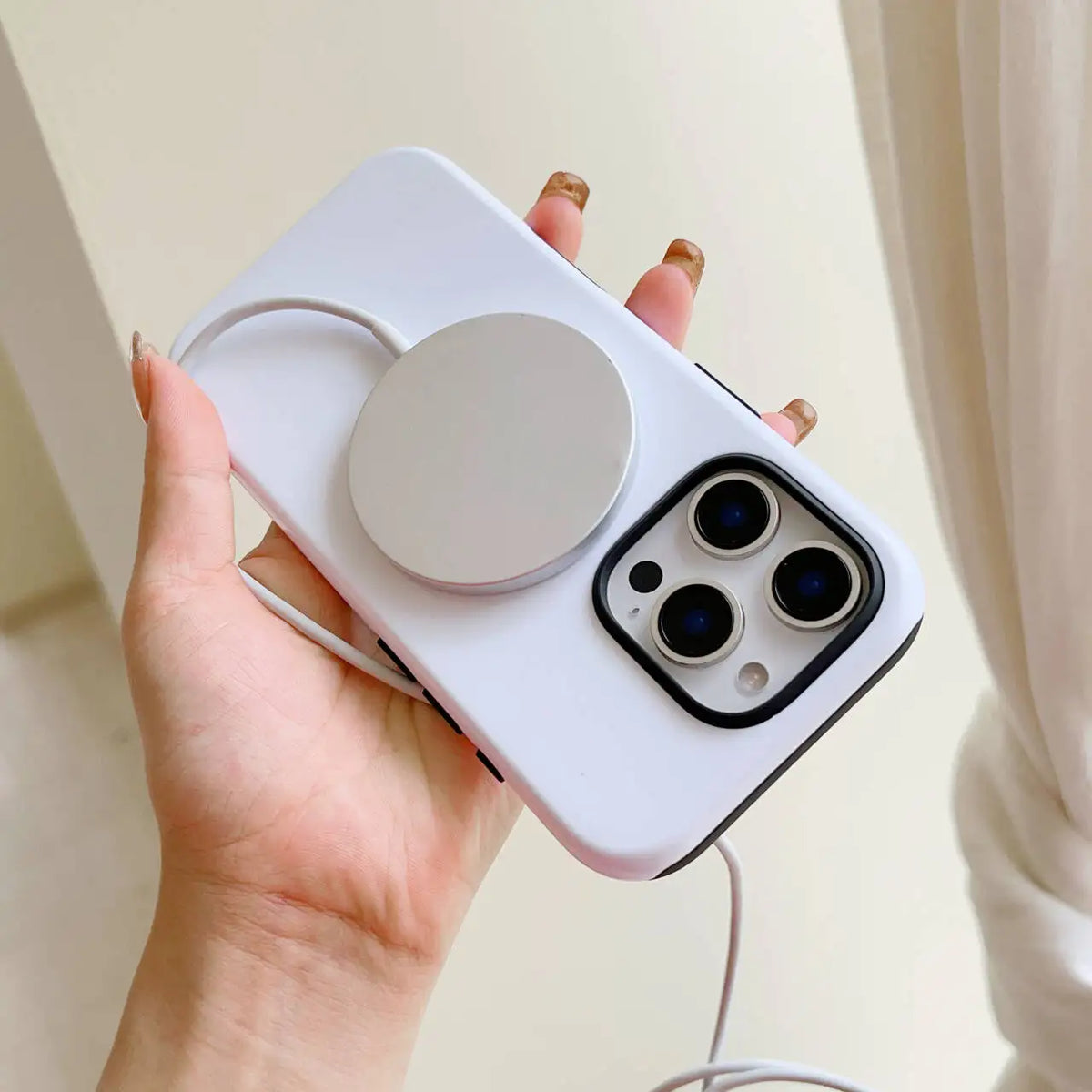 Una mano sostiene una funda de teléfono blanca con lente circular y módulo de cámara, contra un fondo claro.