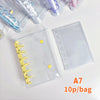 A clear double-button binder with yellow and purple accents is shown next to various colorful pens and a page labeled A7 10p/