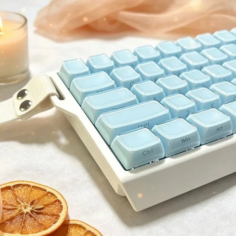 A close-up of light blue crystal jelly keycaps on a white mechanical keyboard with a wooden wrist rest and an orange slice ne