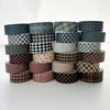 A collection of six rolls of plaid, grid, and polka dot washi tape in various muted tones stacked horizontally.