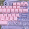 A set of translucent pink jelly keycaps for mechanical keyboards arranged on a clear plastic tray.