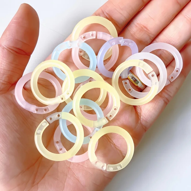 A hand holds several colorful reusable plastic binding rings in various translucent shades.