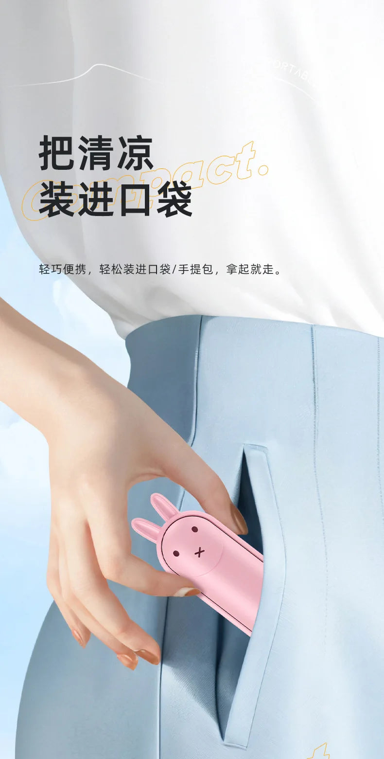 A hand is holding a pink portable foldable rabbit mini fan with a USB charging cable, demonstrating its use.