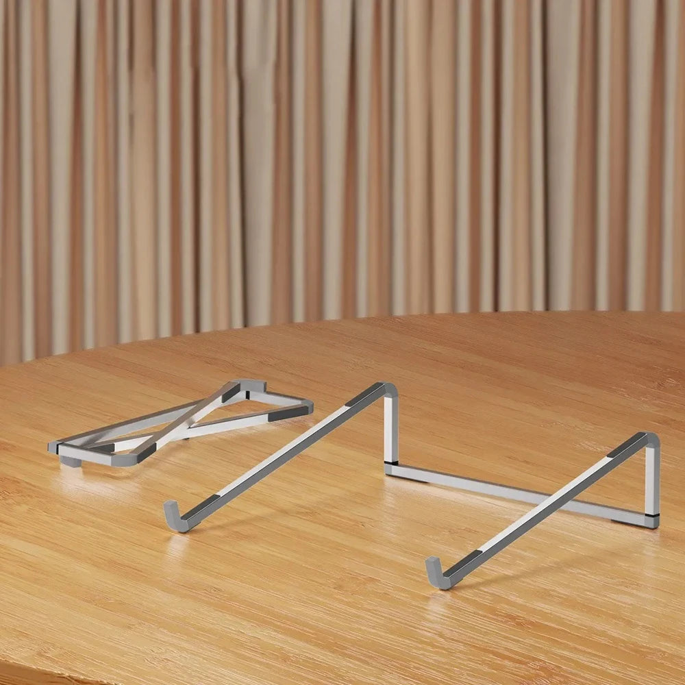 A silver foldable aluminum laptop stand with non-slip grips resting on a wooden table.