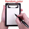 A hand holds a black clipboard with a secure clip, writing on the lined paper with a black pen.