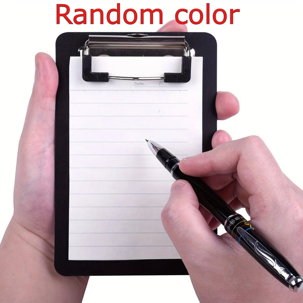 A hand holds a black clipboard with a secure clip, writing on the lined paper with a black pen.