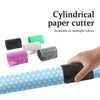 A hand is using a cylindrical paper cutter with various colored plastic cutters on a roll of patterned wrapping paper.
