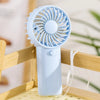 A light blue portable rechargeable mini handheld fan with a circular grille is shown resting on a wooden structure.