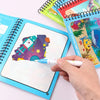 A hand draws a colorful cartoon design in a blue spiral notebook alongside other drawing and coloring notebooks.