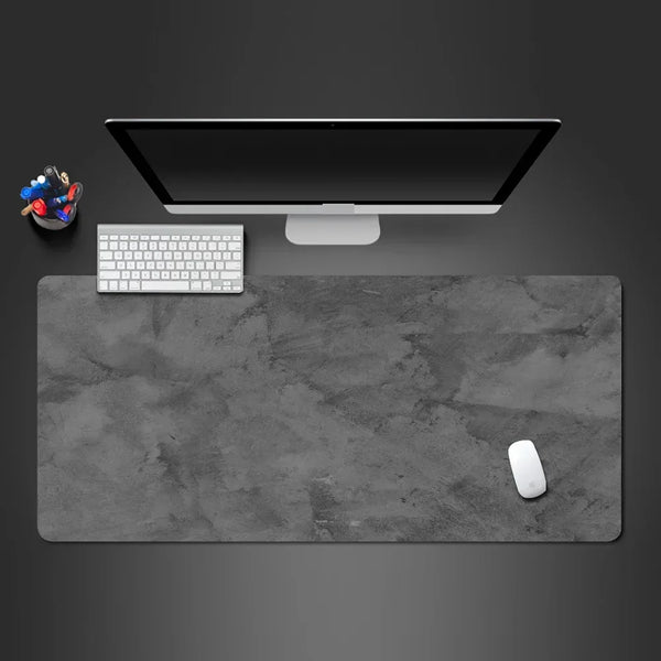 A gray overlocked mouse pad is shown with a computer monitor, keyboard, and mouse on a dark surface.