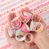 A hand holds a set of pink and floral patterned washi tape rolls on a pink and white patterned cloth.