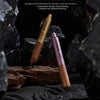Pluma de madera marrón con clip dorado sobre una superficie oscura texturizada rodeada de rocas negras.