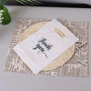 A white thank you gift bag with a woven handle is placed on top of crumpled newspaper.