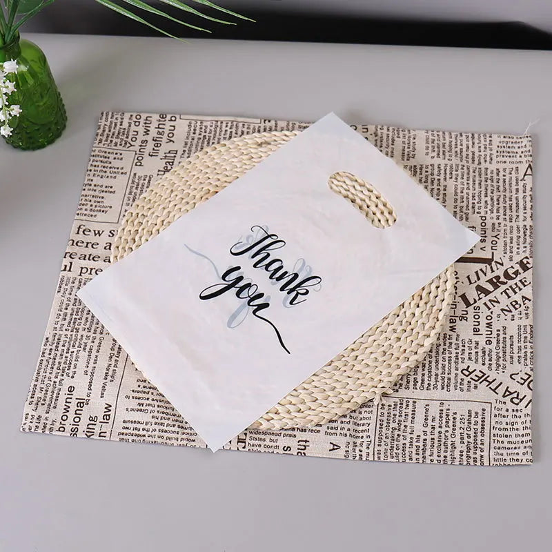 A white thank you gift bag with a woven handle is placed on top of crumpled newspaper.