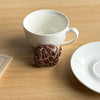 A white ceramic mug and a leopard print earphone case cover are displayed on a wooden surface.