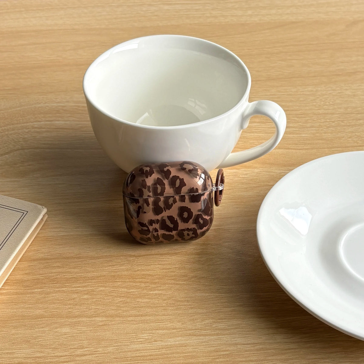 A white ceramic mug and a leopard print earphone case cover are displayed on a wooden surface.