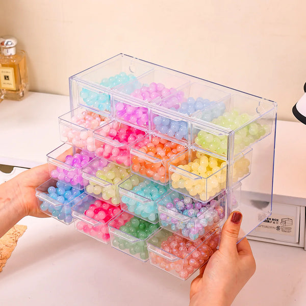 A hand holds an acrylic transparent bead storage box with multiple stackable compartments filled with colorful plastic beads.