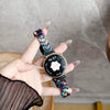 A hand holds a black digital watch with a resin beaded strap and a gold-toned casing against a light gray background.