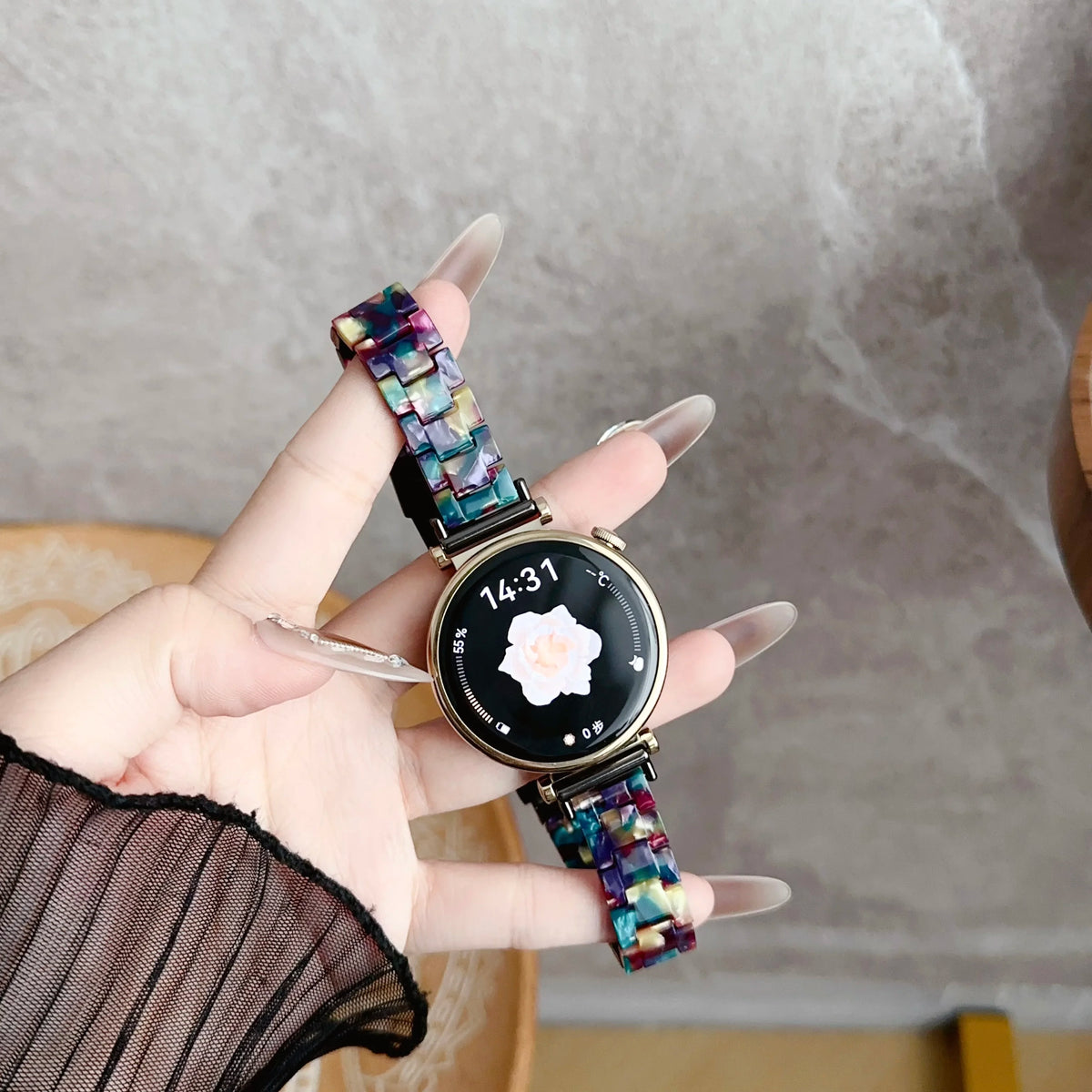 A hand holds a black digital watch with a resin beaded strap and a gold-toned casing against a light gray background.