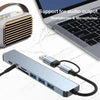 A silver USB hub docking station with multiple ports and cables is shown next to a laptop.