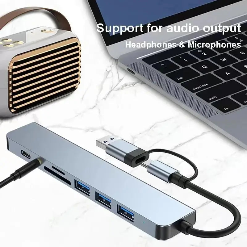 A silver USB hub docking station with multiple ports and cables is shown next to a laptop.