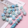 A collection of handmade acrylic flower beads in various shades of blue and teal arranged on a white card.