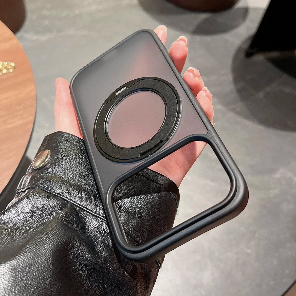 A hand holds a dark gray magnetic phone case with a rotating stand feature.