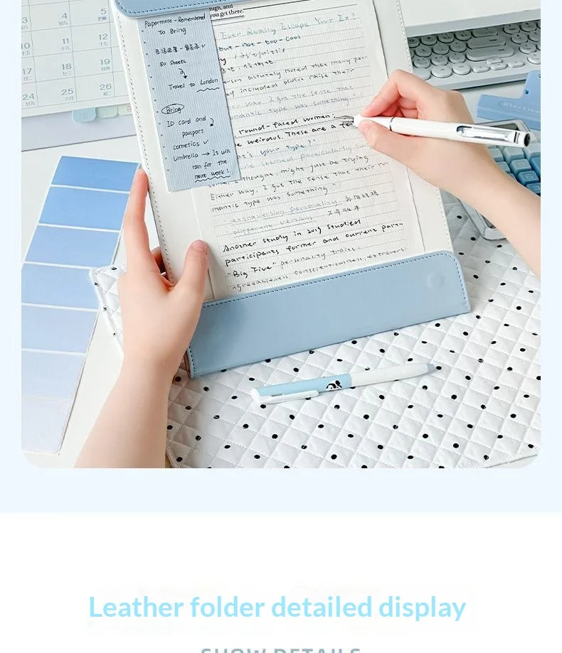 A close-up of an A4 leather clipboard with a magnetic closure and contrast stitching being used for writing.