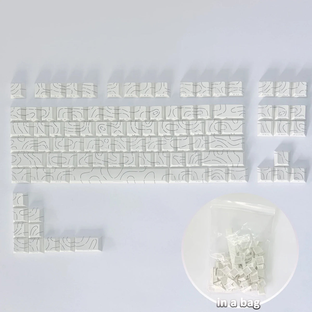 Colección de keycaps de contorno degradado blancos para teclado mecánico, mostradas sobre una superficie blanca.
