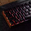 Close-up of a black mechanical keyboard with pink and purple backlit keycaps resting on a dark surface.