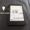 A black Kindle e-reader device is shown on a dark gray surface, with a light bulb icon indicating built-in light.