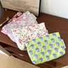 A stack of floral quilted ladies clutch purses in various pink and green patterns resting on a wooden surface.