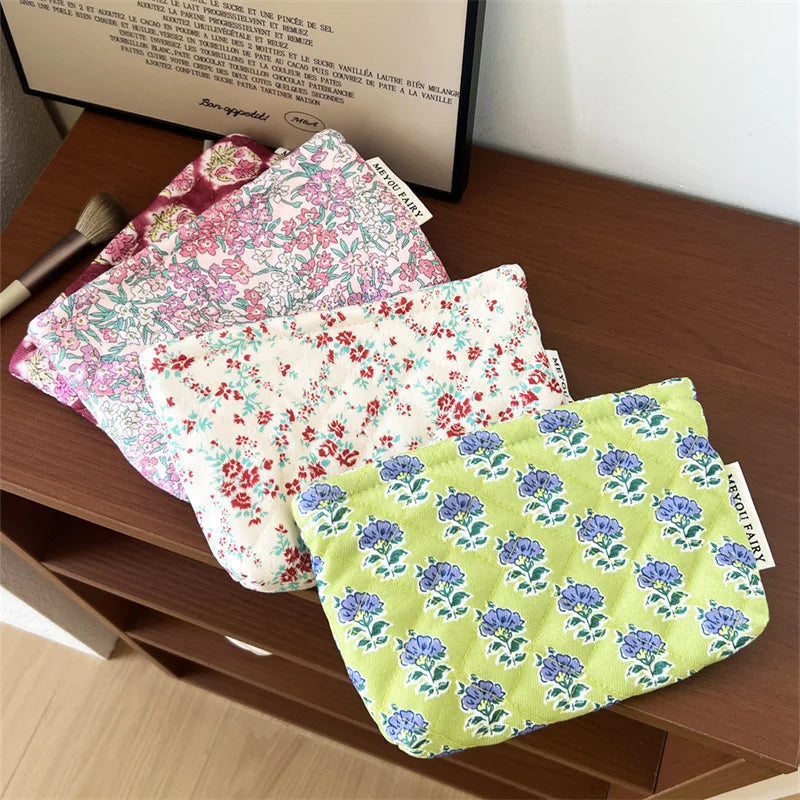 A stack of floral quilted ladies clutch purses in various pink and green patterns resting on a wooden surface.