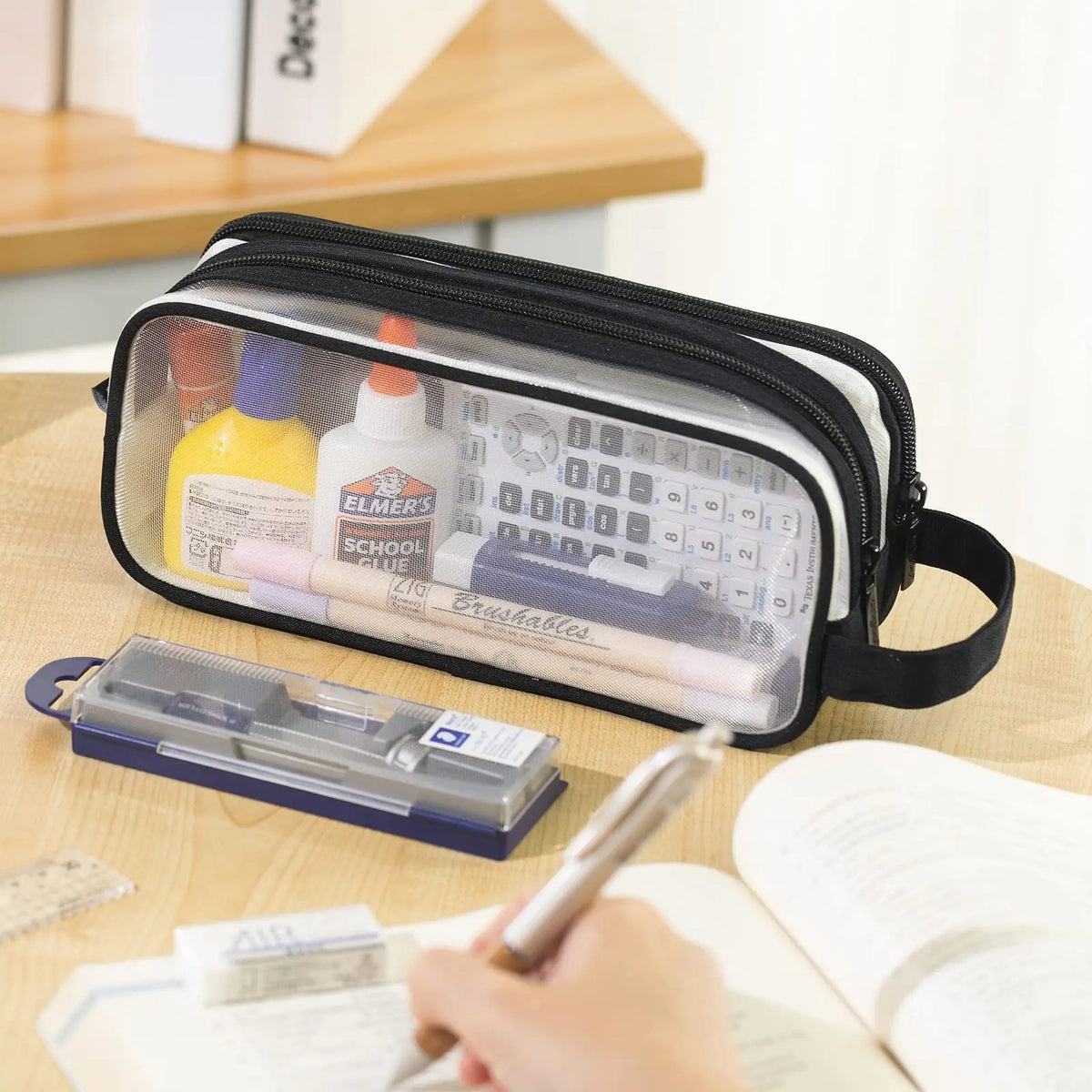 A black transparent mesh pencil pouch is shown next to a notebook and a writing pen.
