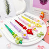 A set of colorful beaded ballpoint pens arranged on a white plate with a potted plant and a pink background.