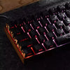 Close-up of a black mechanical keyboard with carbon fiber keycaps and side engraved backlit lettering.
