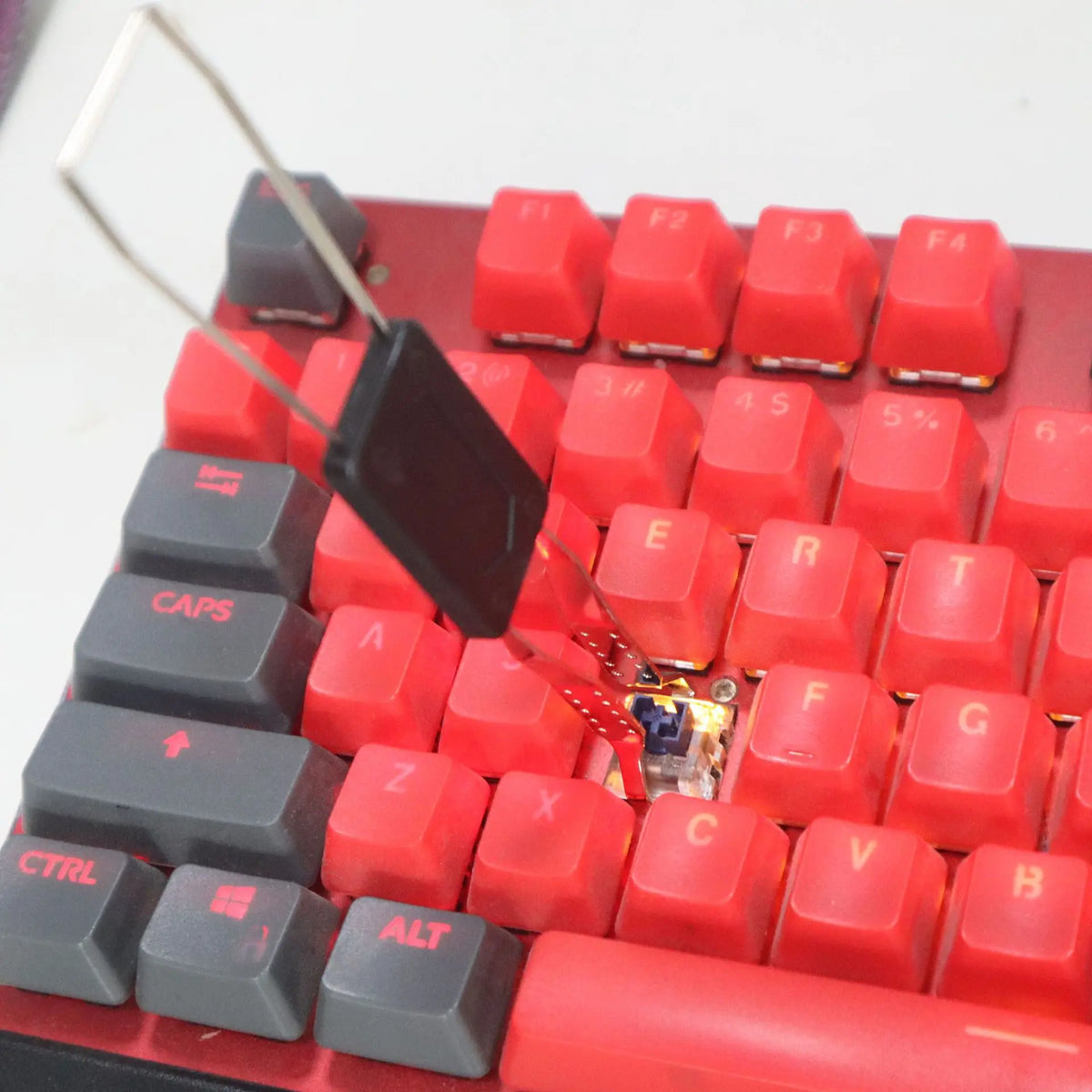 Vista cercana de un teclado mecánico rojo con varias teclas y una herramienta tirador negra.