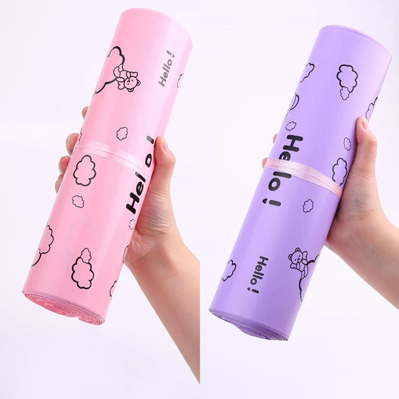 A hand holds a pink reusable plastic mailing bag with a Hello design and a purple reusable plastic mailing bag with a Hello d