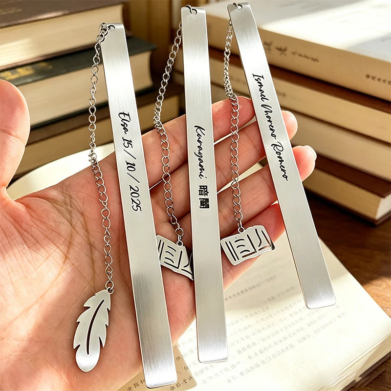 Three stainless steel bookmarks with engraved text and leaf shapes are displayed on a hand against a background of books.
