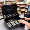 A hand opens a black secure metal money box with a key, revealing stacks of cash inside.