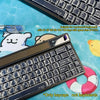 A close-up view of a black mechanical keyboard featuring colorful comic style keycaps and a light-colored keycap set.