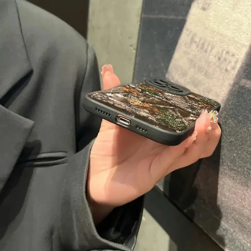 Une main tient une coque de téléphone en silicone noire à motif camouflage de forêt sur un iPhone.