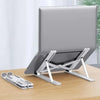 A silver portable folding laptop stand is shown on a wooden desk, ready to support a laptop.