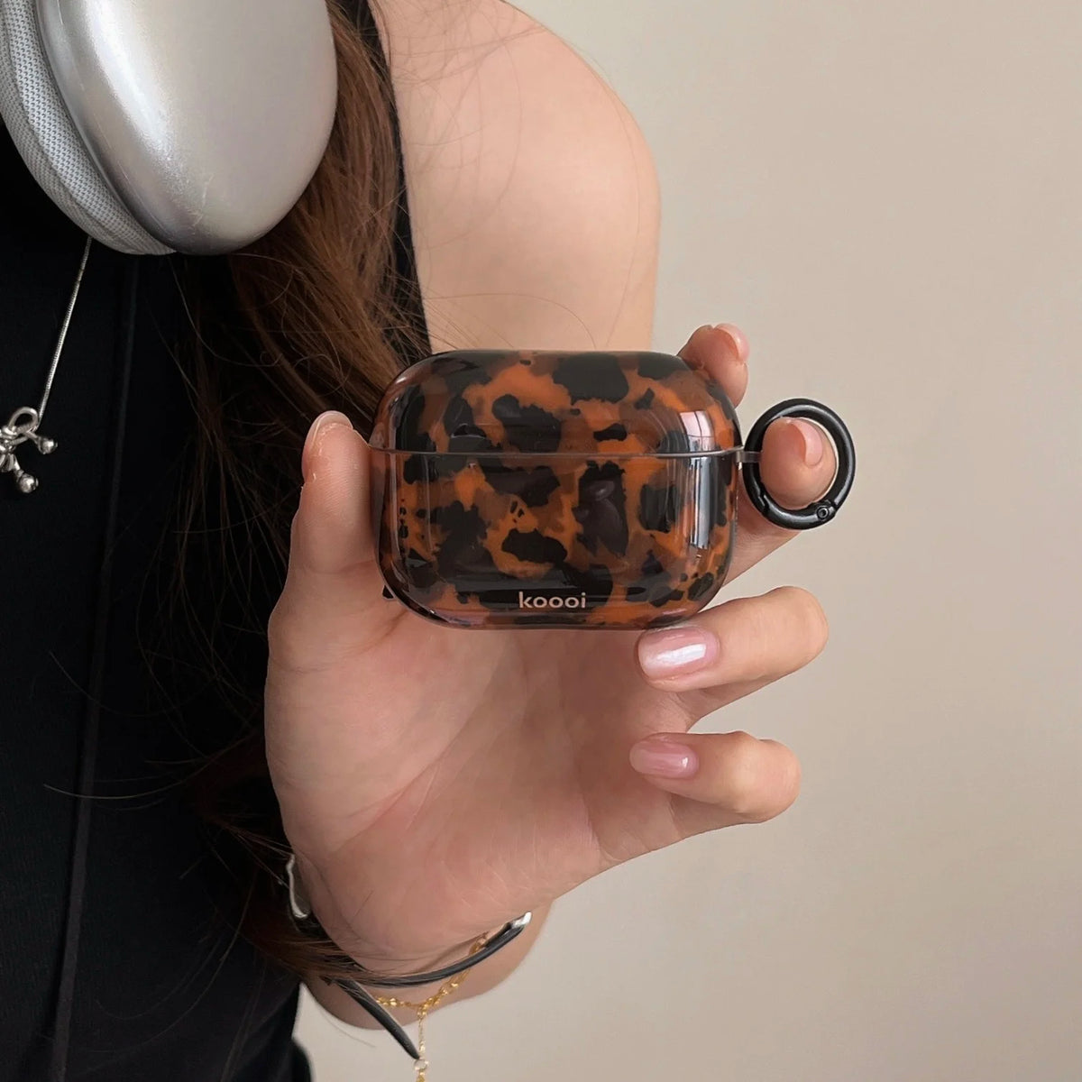 A hand holds a glossy tortoiseshell patterned protective case for AirPods against a light background.