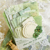 A stack of vintage green paper sheets and a wooden stamp are shown with lace fabric in the background.